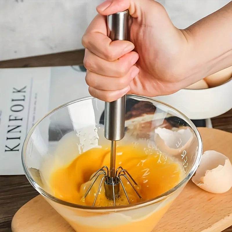 Manual stainless-steel eggbeater mixing eggs in a glass blow 
