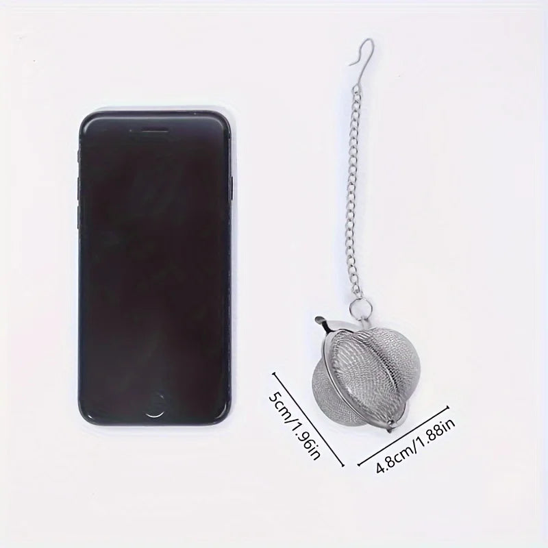 Stainless steel tea infuser ball with hanging chain shown beside a smartphone for size comparison 